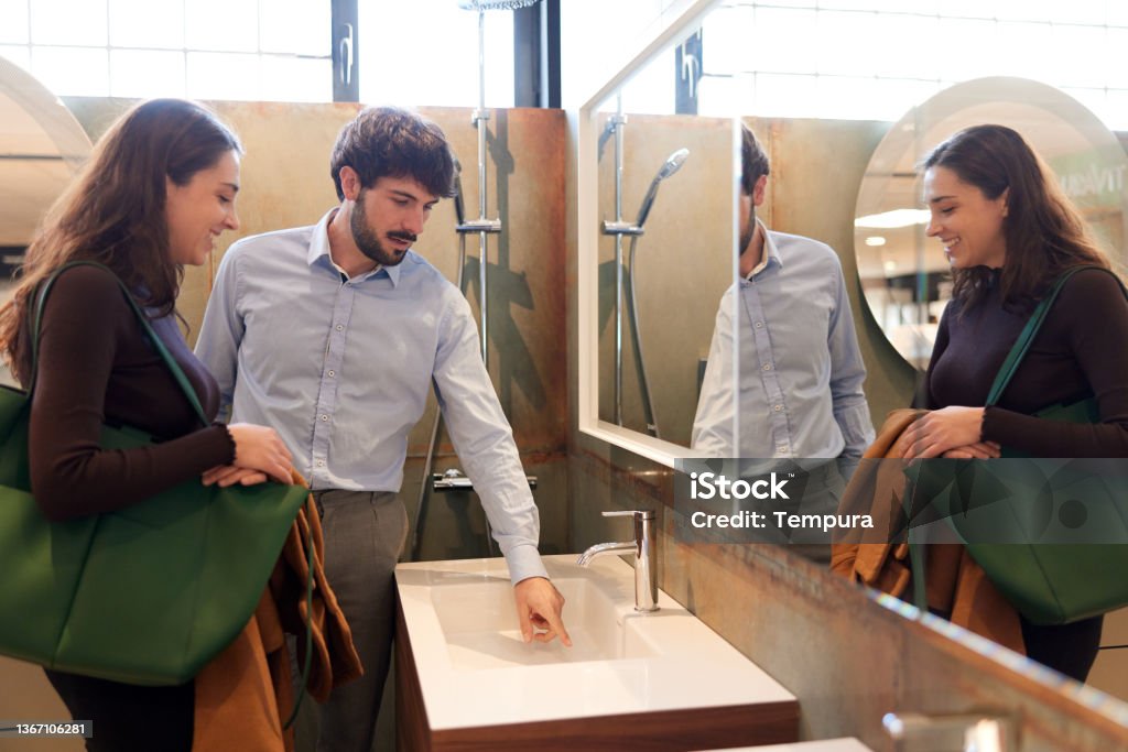 A couple is buying equipment for a new bathroom. A couple is standing next to the sink in a decoration store. Bathroom Stock Photo