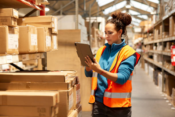 A warehouse worker takes inventory in the storage room. A warehouse worker is standing next to a shelf and using a digital tablet. warehouse containers stock pictures, royalty-free photos & images