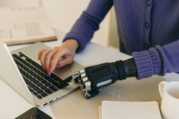 istock Crop shot of female typing on keyboard in artificial bionic arm prosthesis, dressed in veri peri cardigan, sitting at table desk working online, studying, sending e-mail. Biomedical engineering 1367106588