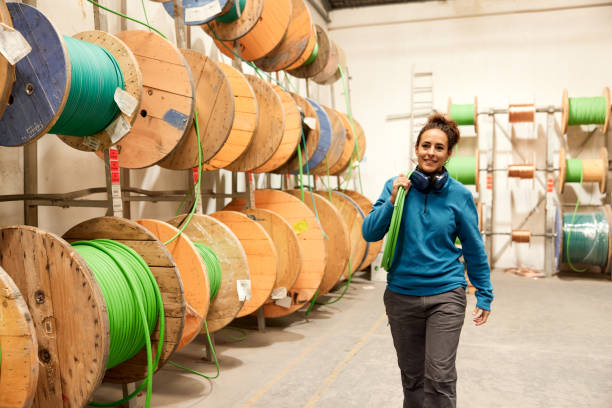 A female blue-collar worker carries an electric cable. A full-length view of a woman carrying an industrial electric cable. wooden spool stock pictures, royalty-free photos & images