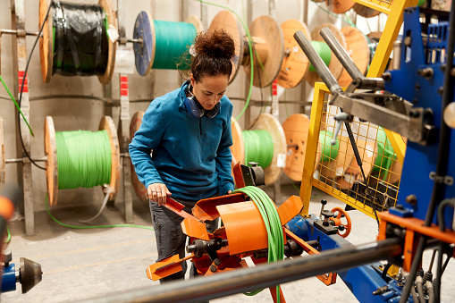 A female worker is rolling and cutting an electric cable with a machine.