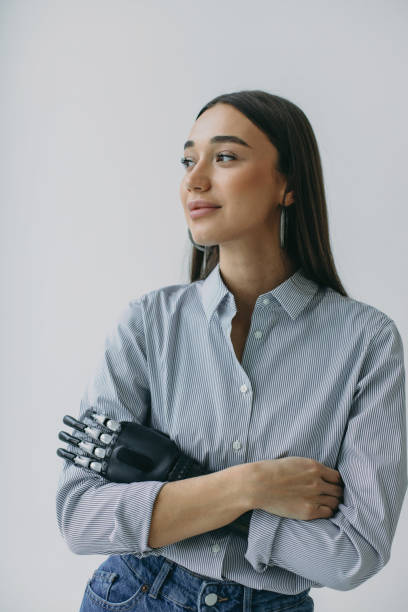 portrait en studio intérieur d’une charmante cyborg féminine photogénique avec un bras prothétique artificiel très développé et confortable au lieu d’une main après un accident. biotechnologie du futur. santé - prosthetic equipment photos et images de collection