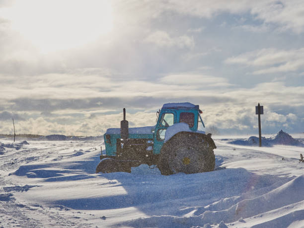 Tractor on a deserted snow-covered field against a cloudy sky. Poor visibility due to a snowstorm.