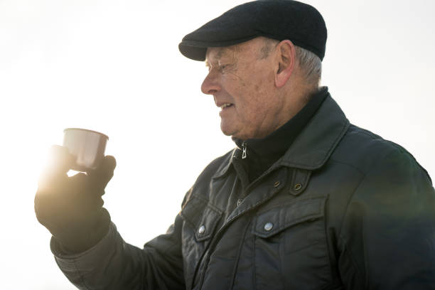 Side View Portrait Senior Man Drinking hot Tea Outdoors on Cold Sunny Winter Day in Rural Landscape, Standing in Backlight