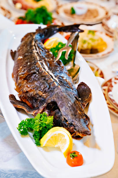 istock baked whole sturgeon on a white platter with lemon, tomato and herbs. 1367113756