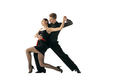 Beautiful sportive young man and woman dancing Argentine tango isolated on white studio background. Artists in black stage costumes. Concept of art, beauty, grace, action, emotions. Copy space for ad