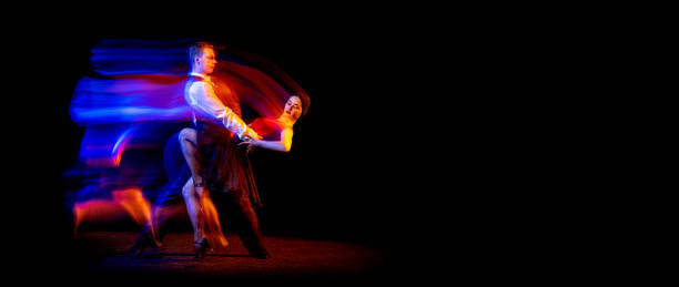 istock Flyer with two young ballroom dancers dancing Argentine tango isolated on dark background with neon mixed light. 1367116541