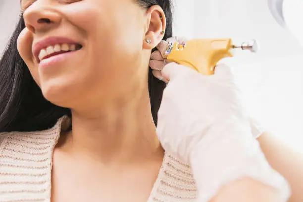 Cropped photo of a smiling woman patient getting ear piercing procedure by a specialist in medical gloves in the cosmetologist cabinet. High quality photo