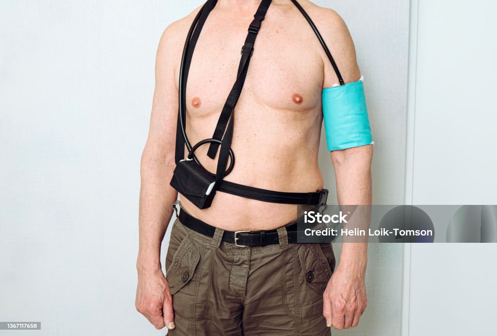 Body of a middle aged man using portable Ambulatory Blood Pressure Monitor (ABPM) for taking measurements during normal daily activities at home. Blood Pressure Gauge Stock Photo