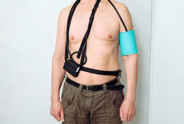 Body of a middle aged man using portable Ambulatory Blood Pressure Monitor (ABPM) for taking measurements during normal daily activities at home.