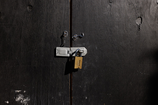 Gold colored padlock locking a wooden door.
