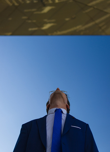 low angle shot of a handsome man wearing formal suit looking up at a golden ceiling with the blue sky behind him.