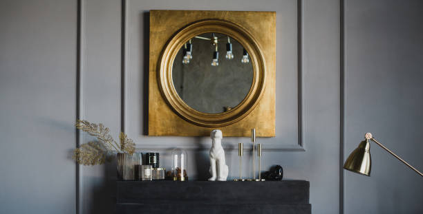 Modern interior with big mirror in golden frame hanging above black decorative fireplace.