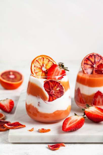 Layered trifle dessert with blood oranges cream Kurd. Layered trifle dessert with blood oranges cream Kurd, greek yogurt, Savoyardi cookies, orange chips and strawberry in serving glasses. Close up, copy space. trifle stock pictures, royalty-free photos & images