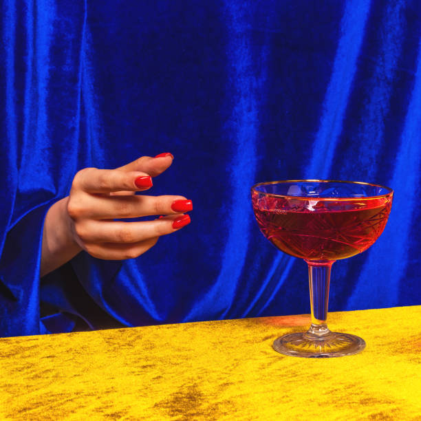 женская рука тянется к бокалу с манхэттенским коктейлем, изолированным на ярко-желто-синем неоновом фоне. понятие вкуса, алкогольные напит� - manhattan cocktail стоковые фото и изображения
