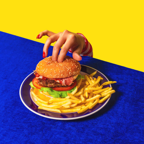 photographie pop art culinaire. main femelle et hamburger, français frites sur nappe bleu vif isolées sur fond jaune. vintage, style rétro - image created 1990s photos et images de collection