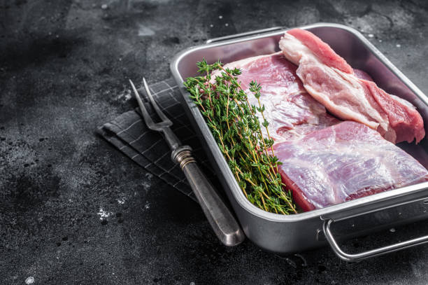 Fresh Raw pork belly with skin in a steel tray with herbs. Black background. Top view. Copy space Fresh Raw pork belly with skin in a steel tray with herbs. Black background. Top view. Copy space. berkshire pig stock pictures, royalty-free photos & images