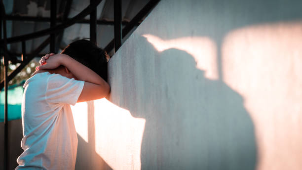 Asian preteen boy standing and leaning head against wall at home, hand cover face, feeling depressed and frustrated. Asian teen boy standing in backyard at home, leaning head against wall, hand cover face, feeling depressed and frustrated. Evening light cast shadow on wall. face down stock pictures, royalty-free photos & images