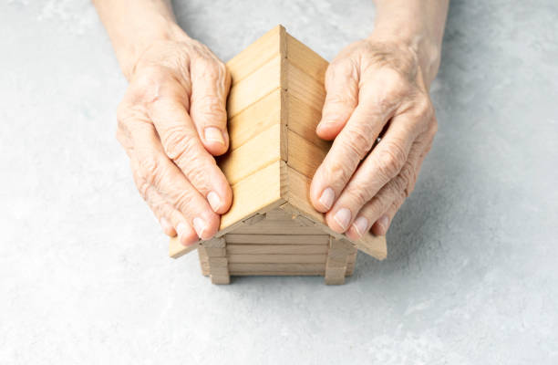 Wrinkled hands of an elderly woman protects the house. Taking care of your home concept. stock photo