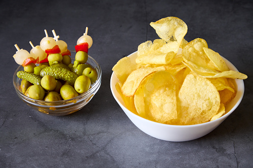 A white bowl with chips and a glass bowl with Spanish brochette on a black slate background