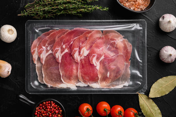 Vacuum packed serrano ham, on black dark stone table background, top view flat lay