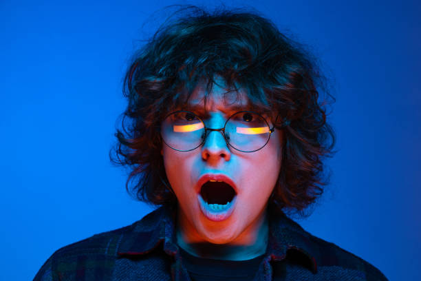 istock Shocked young man, student with open mouth looking at camera isolated on blue background in neon. Concept of emotions, study, education, fashion 1367136943