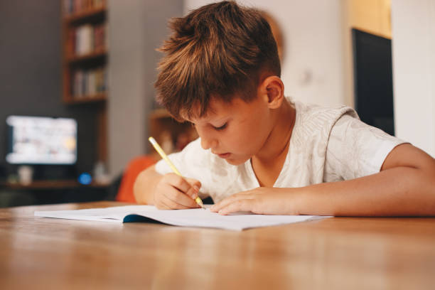 istock A right-handed boy is sitting at the table, writing down in his notebook. 1367137079