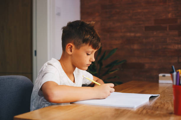 istock A young boy, elementary-age, is sitting at the table in the dining room. He has a notebook in front of him, writing in it. 1367137090