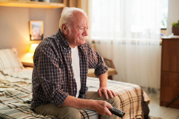 istock Old man with remote control choosing channel while watching tv 1367139881