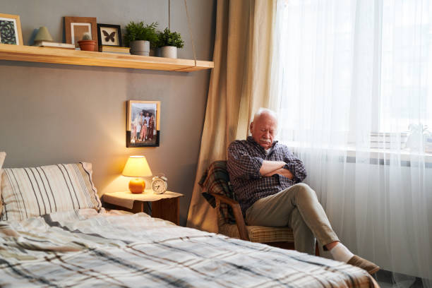 Tired senior man sitting in armchair by window and napping Tired senior man sitting in armchair by window and napping in the middle of day in front of double bed in home environment man sleeping chair stock pictures, royalty-free photos & images