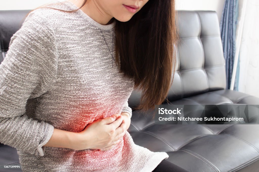 Asian woman is stomached and use hand cross stomach and feeling pain with an inflaming Asian woman is stomached and use hand cross stomach and feeling pain with inflaming Norovirus Stock Photo