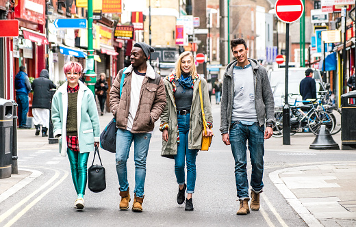 Multicultural students walking on Brick Lane center at Shoreditch London - Life style concept with multi-ethnic young friends on seasonal clothes having fun together outside - Bright vivid filter