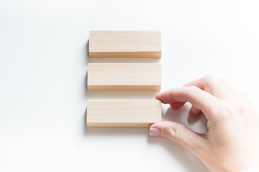 Blank three wooden blocks on a white background and a person's hand lays out the blocks