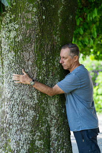 Latino man from Bogota Colombia between 50 and 59 years old, hugs a tree as a treatment for anxiety
