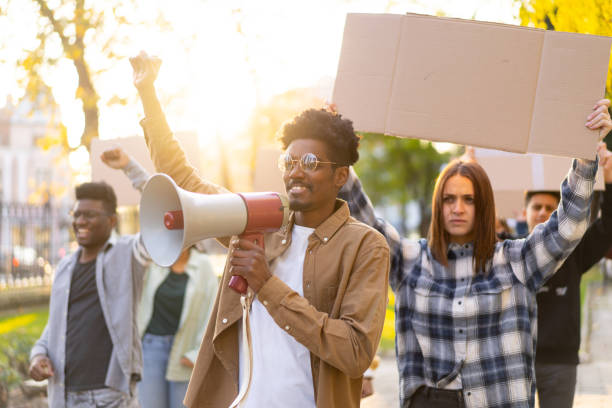 Students demonstrating with blank placards A group of activists holding blank banners in the air while their leader uses a megaphone, in a public park on a sunny day social justice concept photos stock pictures, royalty-free photos & images