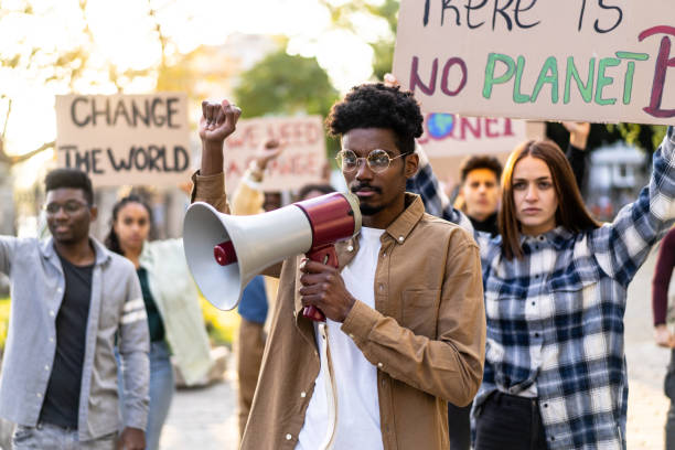 A young man using a megaphone during a environmental protest An African-American man holds a megaphone during a student protest about climate change, his friends are holding placards with their messages to change the world climate crisis photos stock pictures, royalty-free photos & images