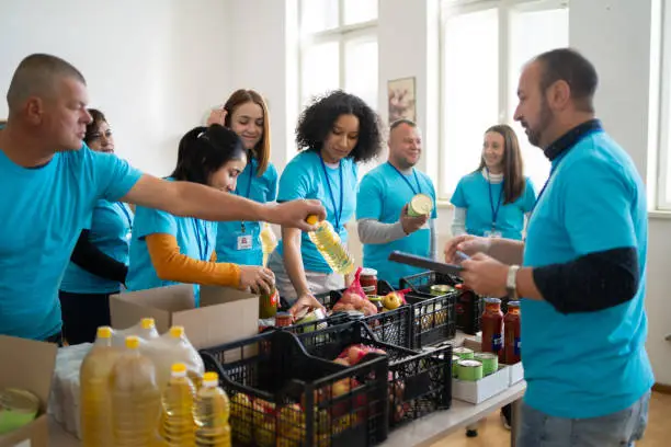 Multi-racial volunteers are packing food donation boxes in a food bank, wearing matching t-shirts