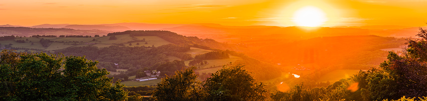 Warm lights of sunset illuminating the wooded hills and steep valleys, mountain ridges and rural homes of the Wye Valley from Herefordshire into South Wales, UK.