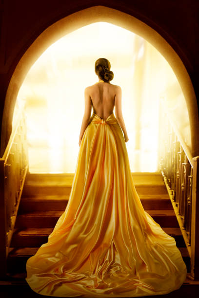 damensilhouette im goldenen luxuskleid. elegante dame im gelben langen seidenkleid mit nackter rückansicht hinten. fantasy fashion model girl schaut auf licht in doorway - dress full length women sensuality stock-fotos und bilder