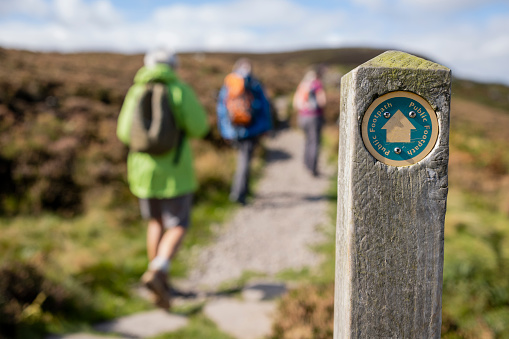 Out of focus shot tourists hiking uphill in Rothbury, Northumberland. The trail post is at the forefront of the shot and is the main focus.