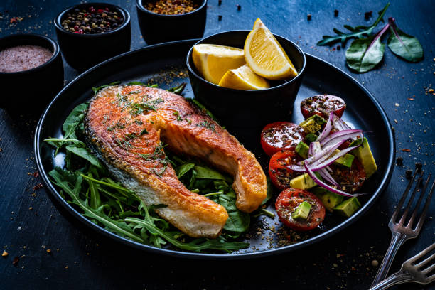 istock Fried salmon steak and fresh vegetables on black wooden background 1367149944