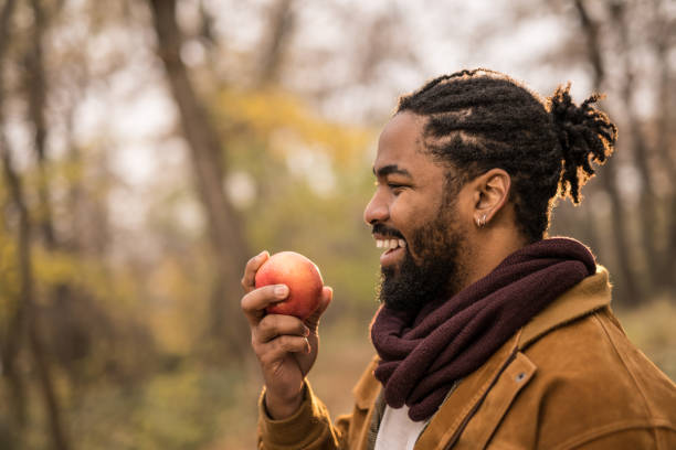istock Happy young African American man eating an apple while on a walk outdoors in nature. 1367150032