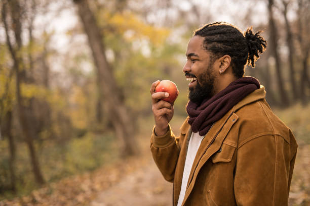 istock Happy young African American man eating an apple while on a walk outdoors in nature. 1367150046