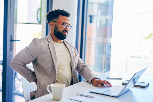 photo d’un jeune homme d’affaires souffrant de maux de dos alors qu’il travaillait dans un bureau moderne au travail - back rear view backache posture photos et images de collection