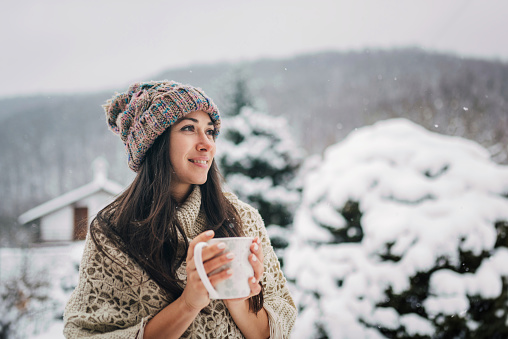 Young caucasian woman enjoying the snowy winter day with a cup of hot tea
