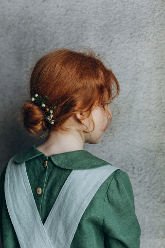 Red-haired girl in linen clothes stands with her back showing details