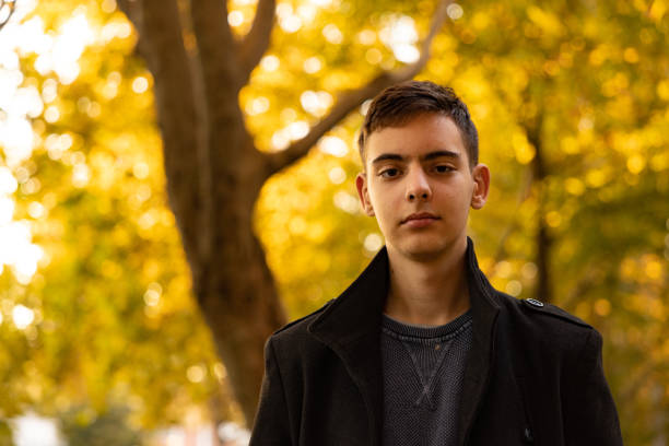 Portrait of a confident 15 year’s old Caucasian teenage boy, in front of  treetop