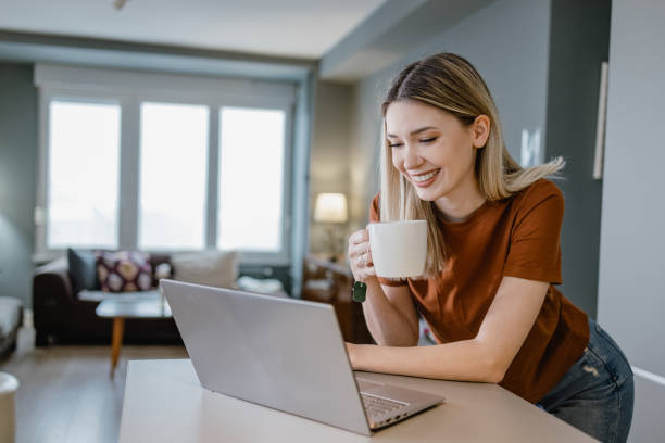 A beautiful young woman uses laptop at home on the kitchen counter stock photo
