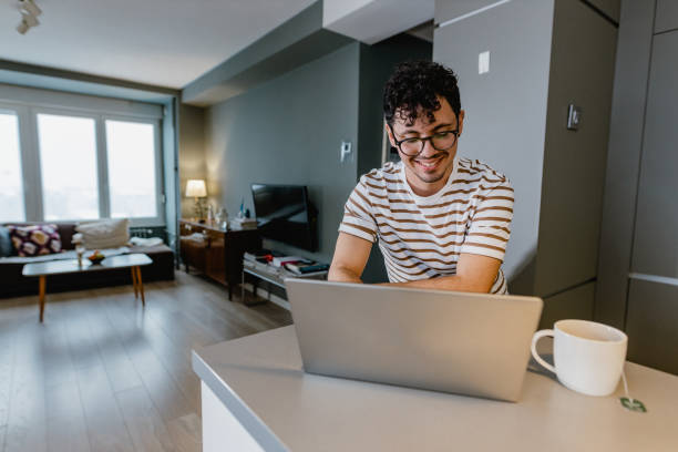 istock Young man uses laptop at home on the kitchen counter 1367155239