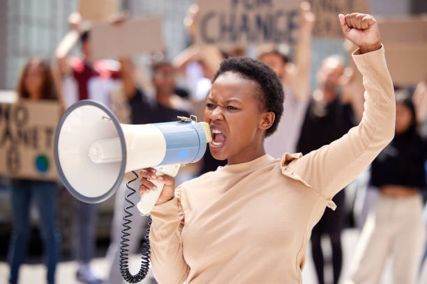 shot of a young woman shouting through a loudhailer at a protest - anti governments imagens e fotografias de stock